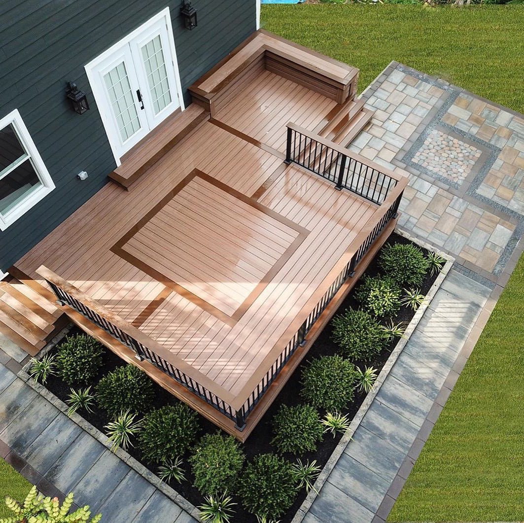 A multi-toned brown wooden deck with black metal railings attached to a dark grey house.