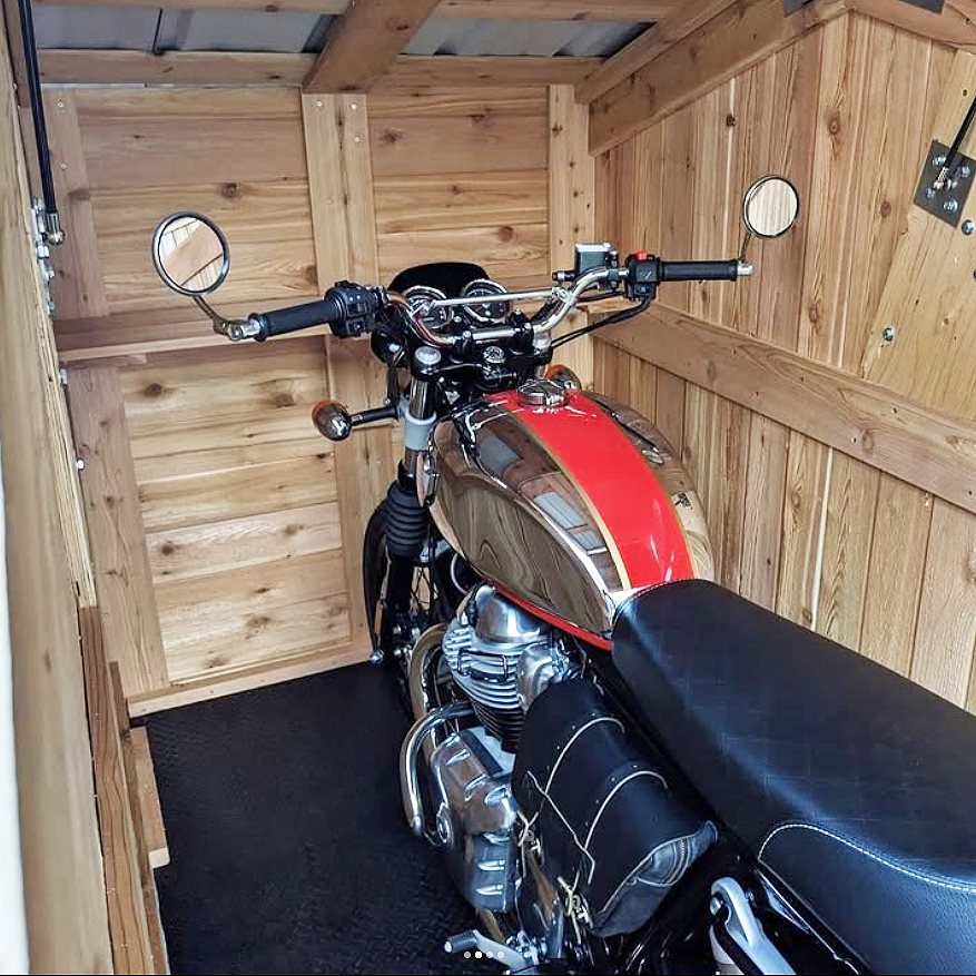 A red and chrome motorcycle parked inside a small wooden storage shed with timber walls.
