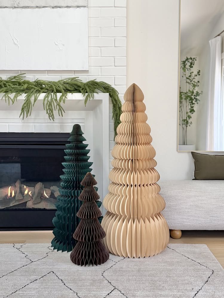 Three honeycomb paper trees in tan, brown, and green standing on a rug.
