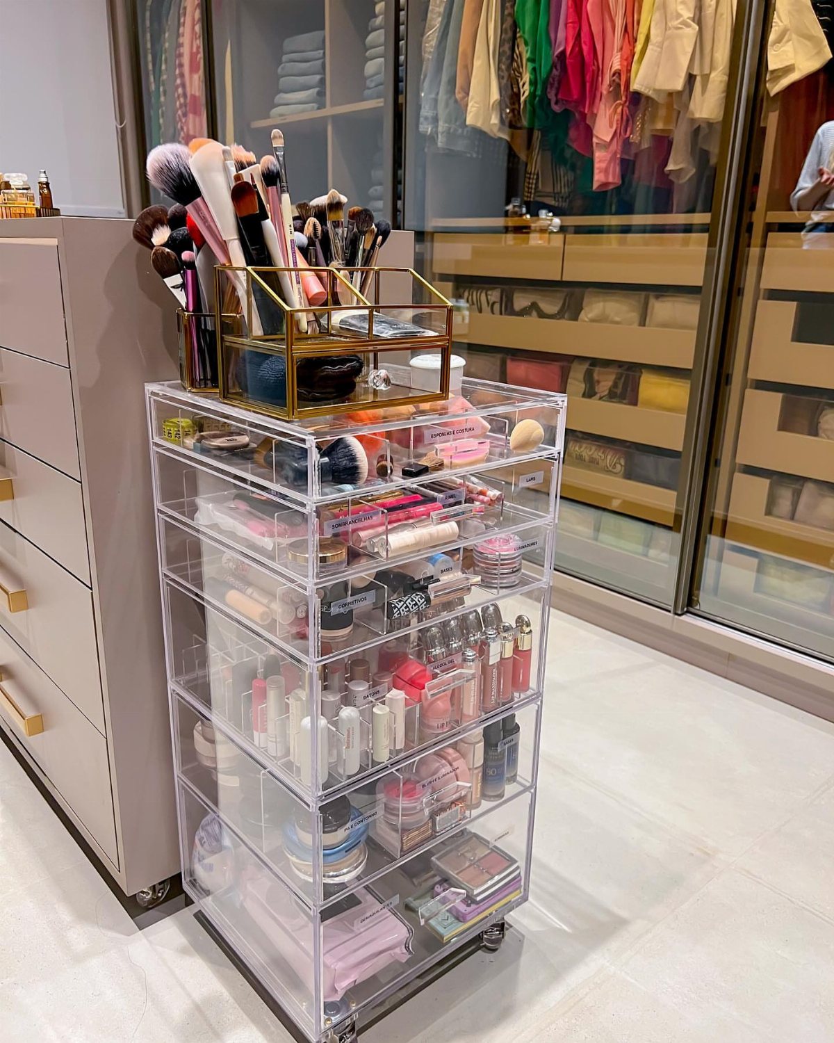 Clear acrylic rolling cart filled with organized makeup products and brushes on top.