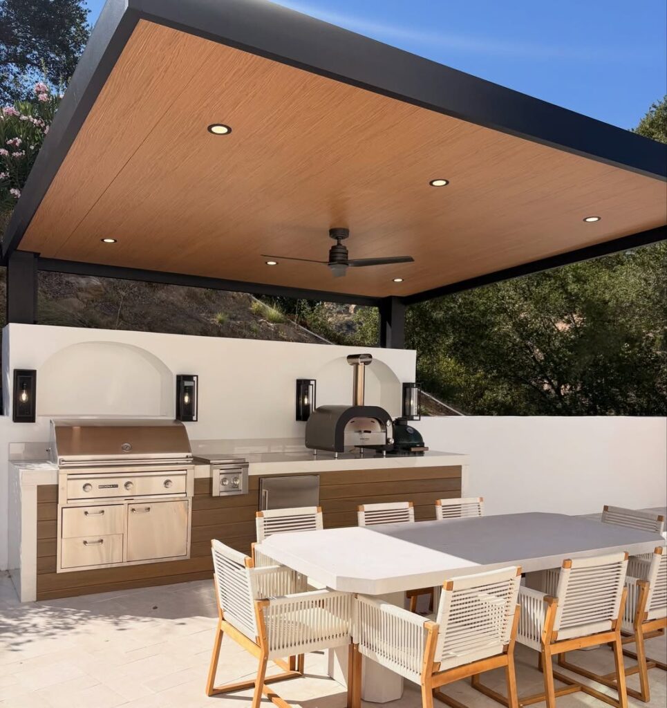 Modern outdoor kitchen with a built-in grill and pizza oven under a covered patio.