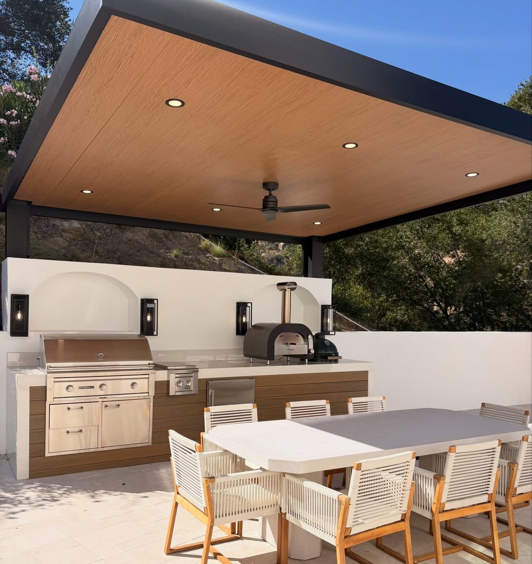 Modern outdoor kitchen with a built-in grill and pizza oven under a covered patio.