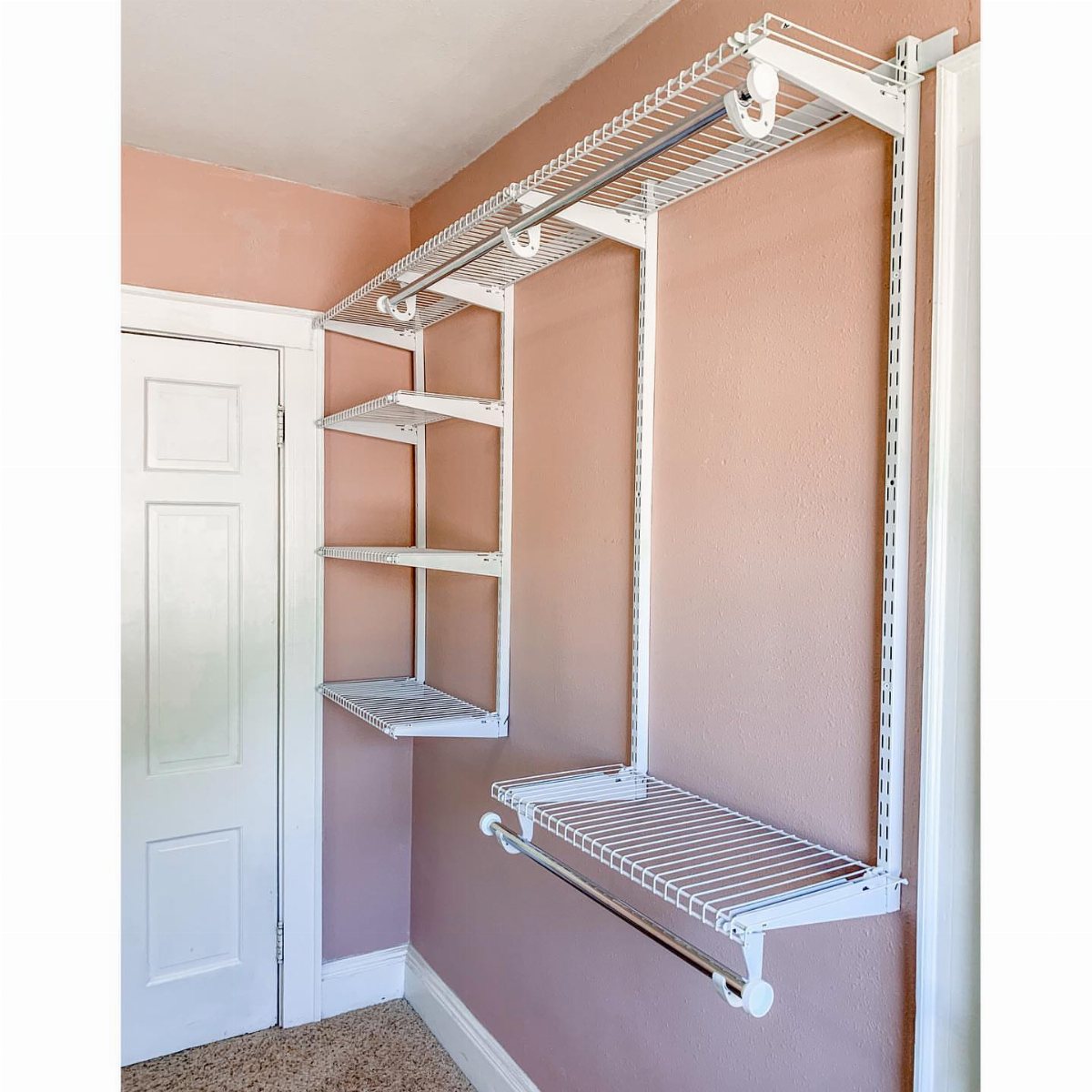 White wire closet organizer system with shelves and hanging rods installed on a peach wall.