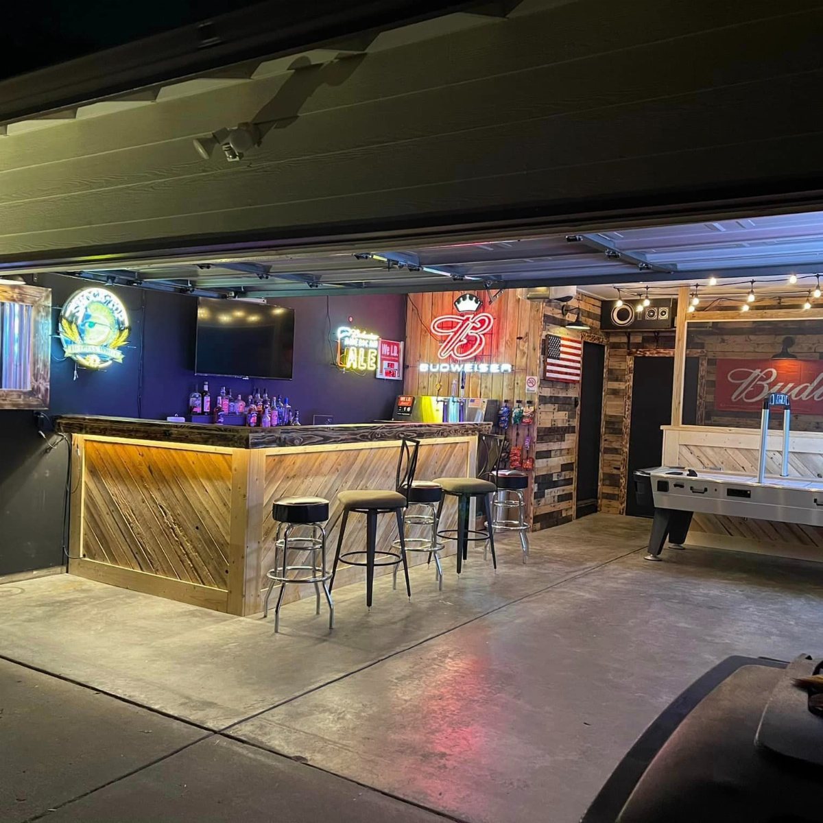 A wooden bar counter with black stools set up inside a garage space.