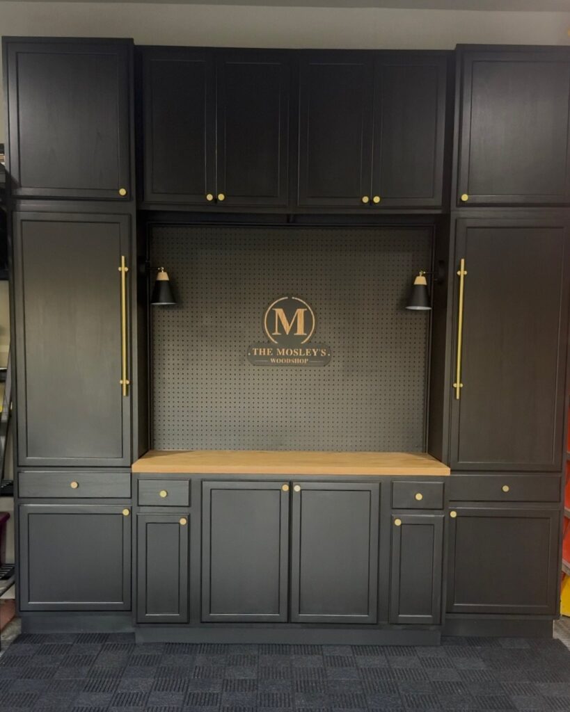 Dark charcoal grey built-in garage cabinets with a central wooden workbench and pegboard backsplash.