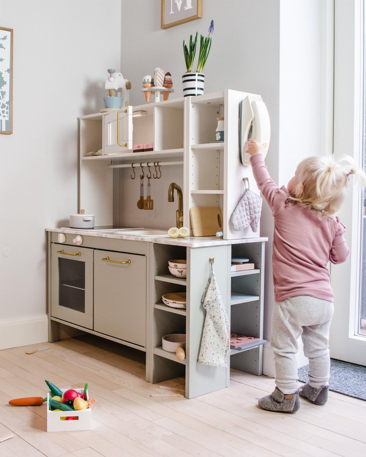 A young child playing with a customized grey and white wooden toy play kitchen.