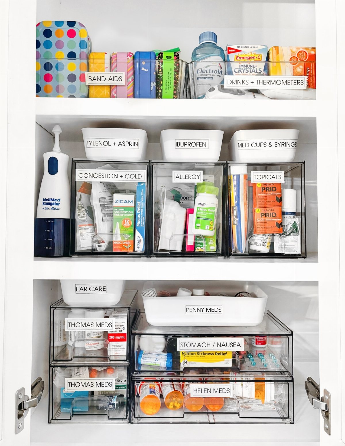 Organized medicine cabinet with clear plastic bins and labeled containers holding various medical supplies and medications.
