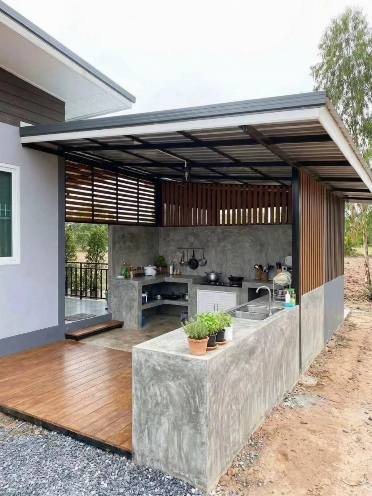 Modern outdoor kitchen featuring concrete countertops, a built-in sink, and wooden slat accents under a metal roof.