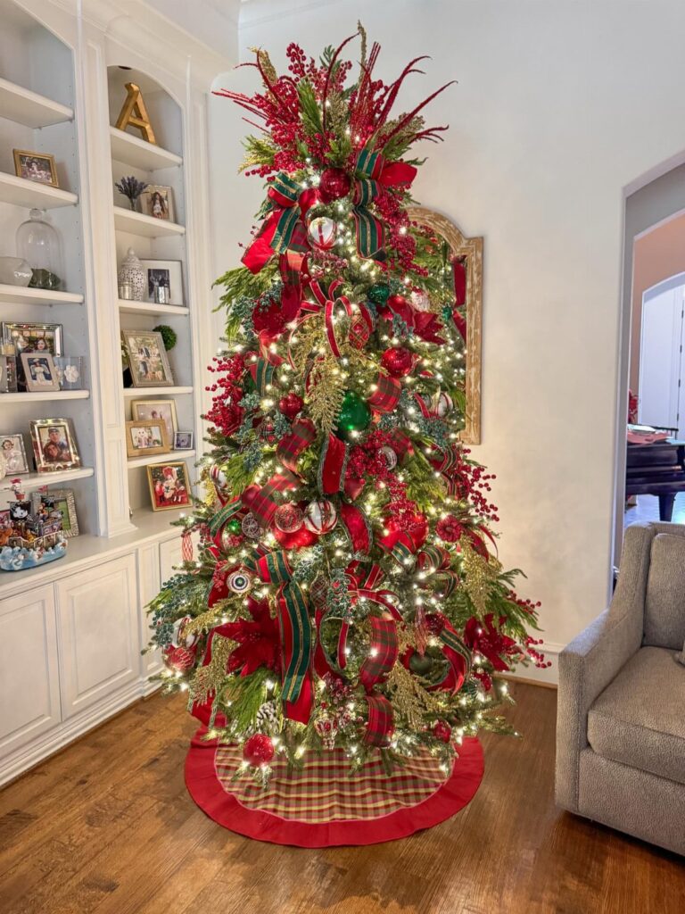 A decorated Christmas tree with red and green ornaments and lights in a living room.