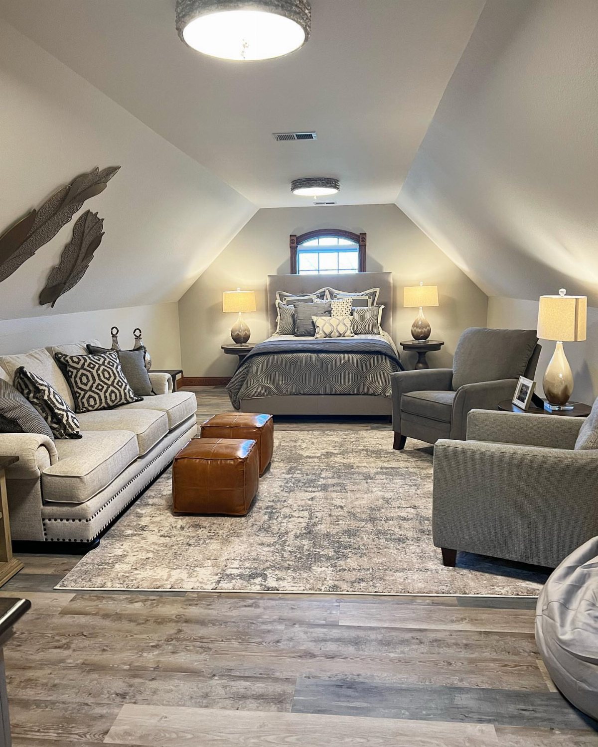 A furnished attic living space with a bed, sofa, armchairs, and patterned rug.