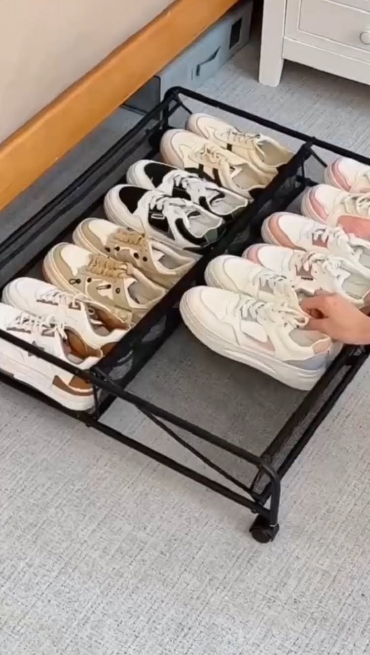 Black metal rolling storage tray filled with various sneakers on a grey carpeted floor.