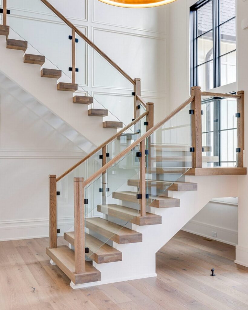 Modern wooden staircase with glass railings and black metal hardware in a bright room.
