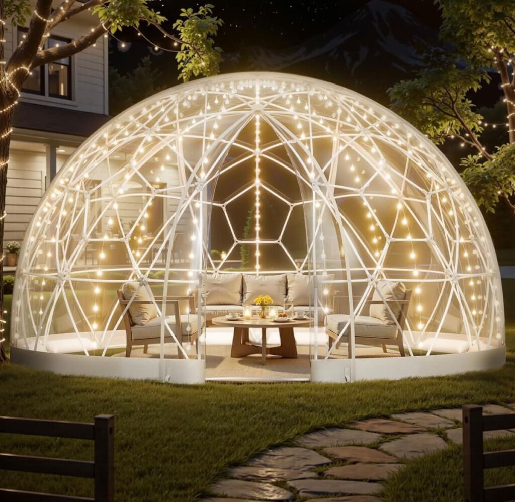A glowing transparent geodesic dome with string lights and outdoor furniture on a lawn at night.