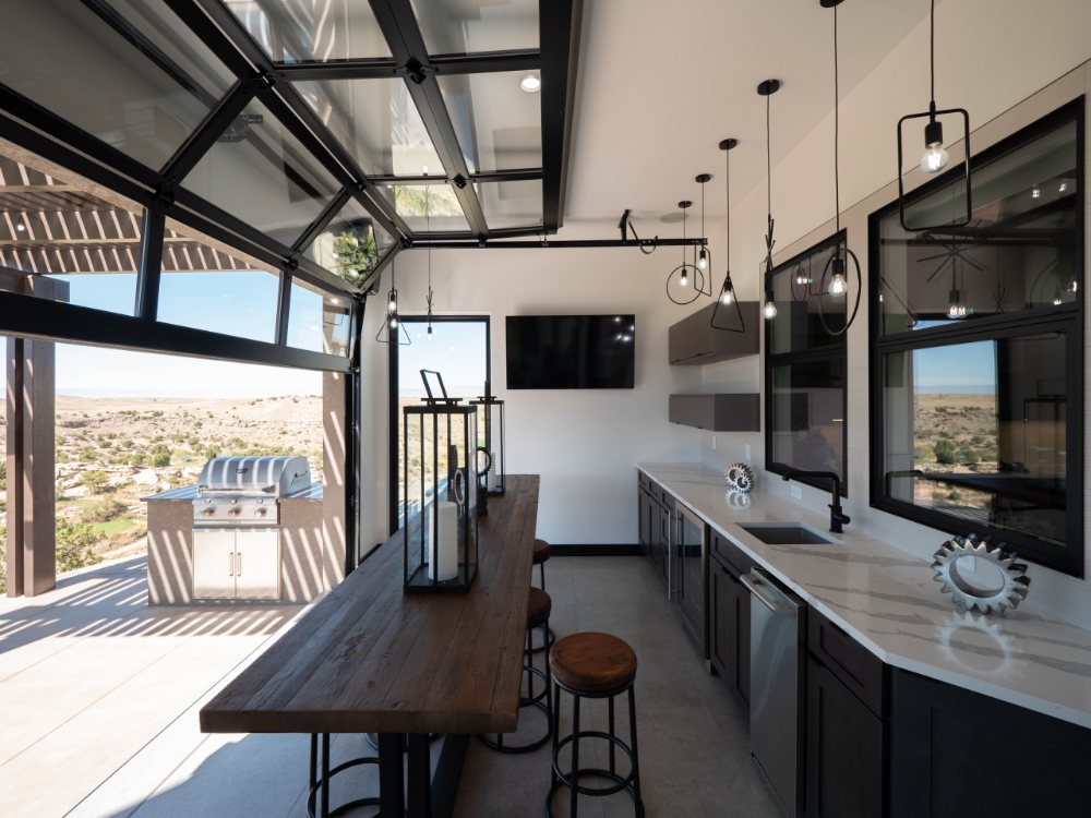 Modern kitchen with a large glass garage door opening onto an outdoor patio and grill.