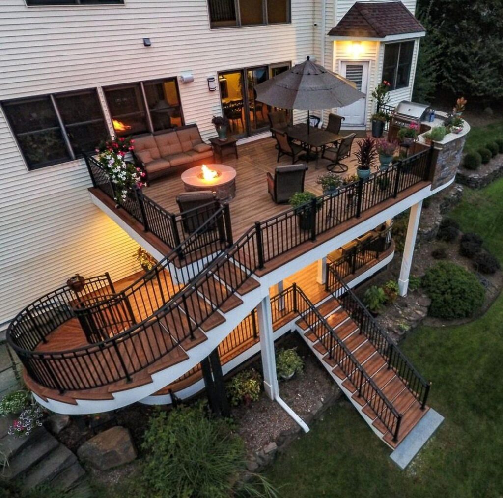 A multi-level wooden deck with black railings, curved stairs, and outdoor furniture attached to a house.