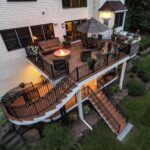 A multi-level wooden deck with black railings, curved stairs, and outdoor furniture attached to a house.