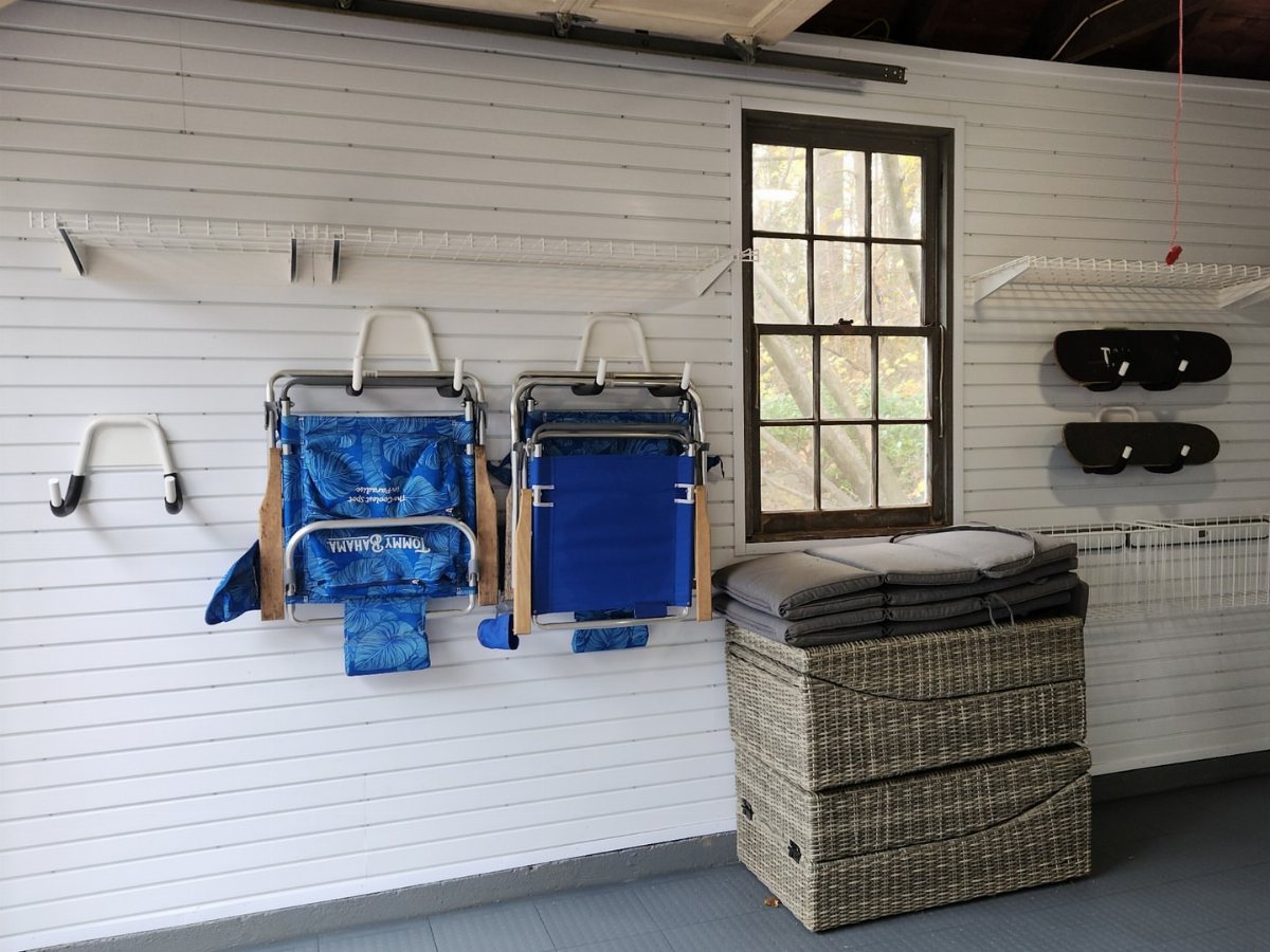 Blue camping chairs hanging from white wall hooks in a garage storage setup.