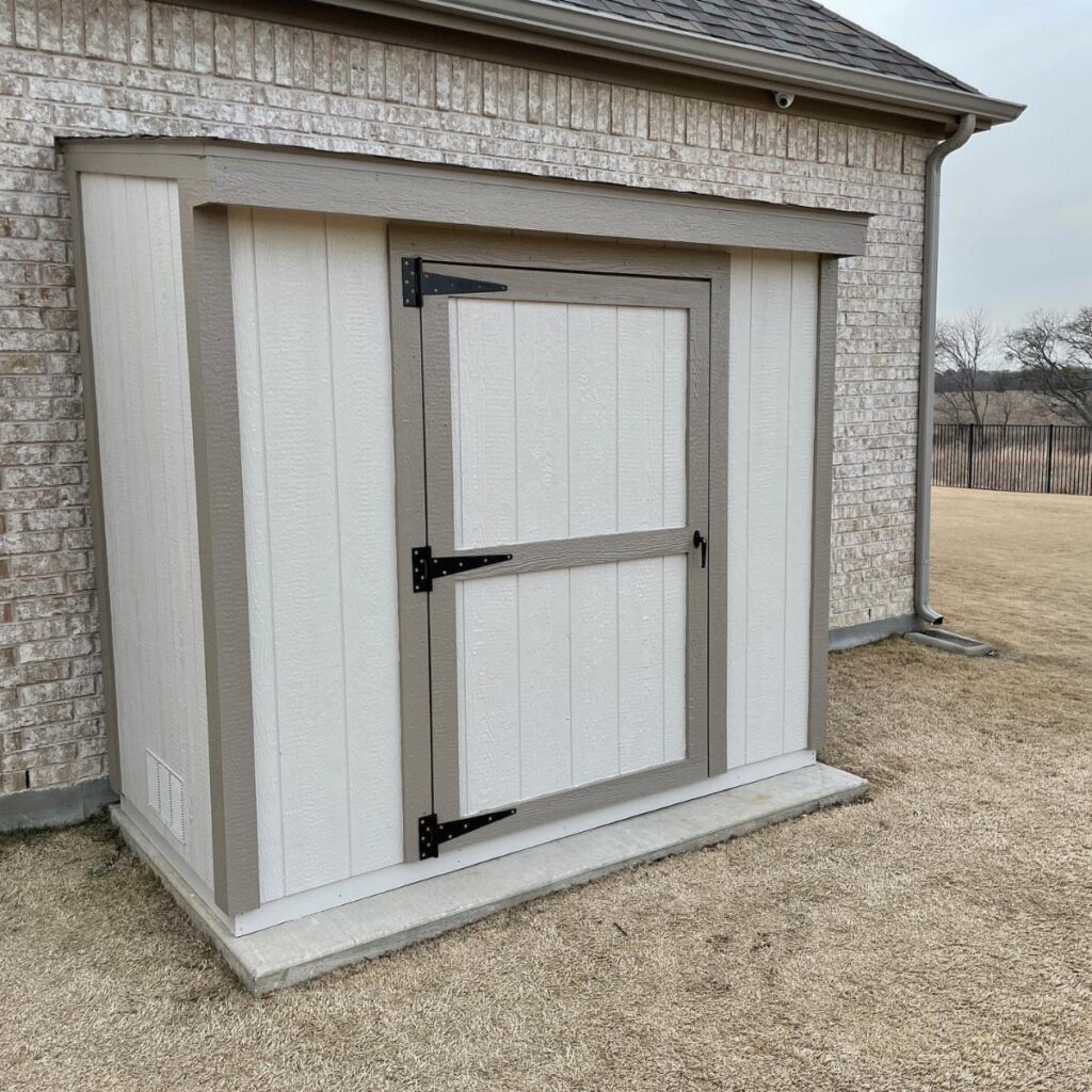 A white lean-to shed with tan trim attached to a brick building wall.