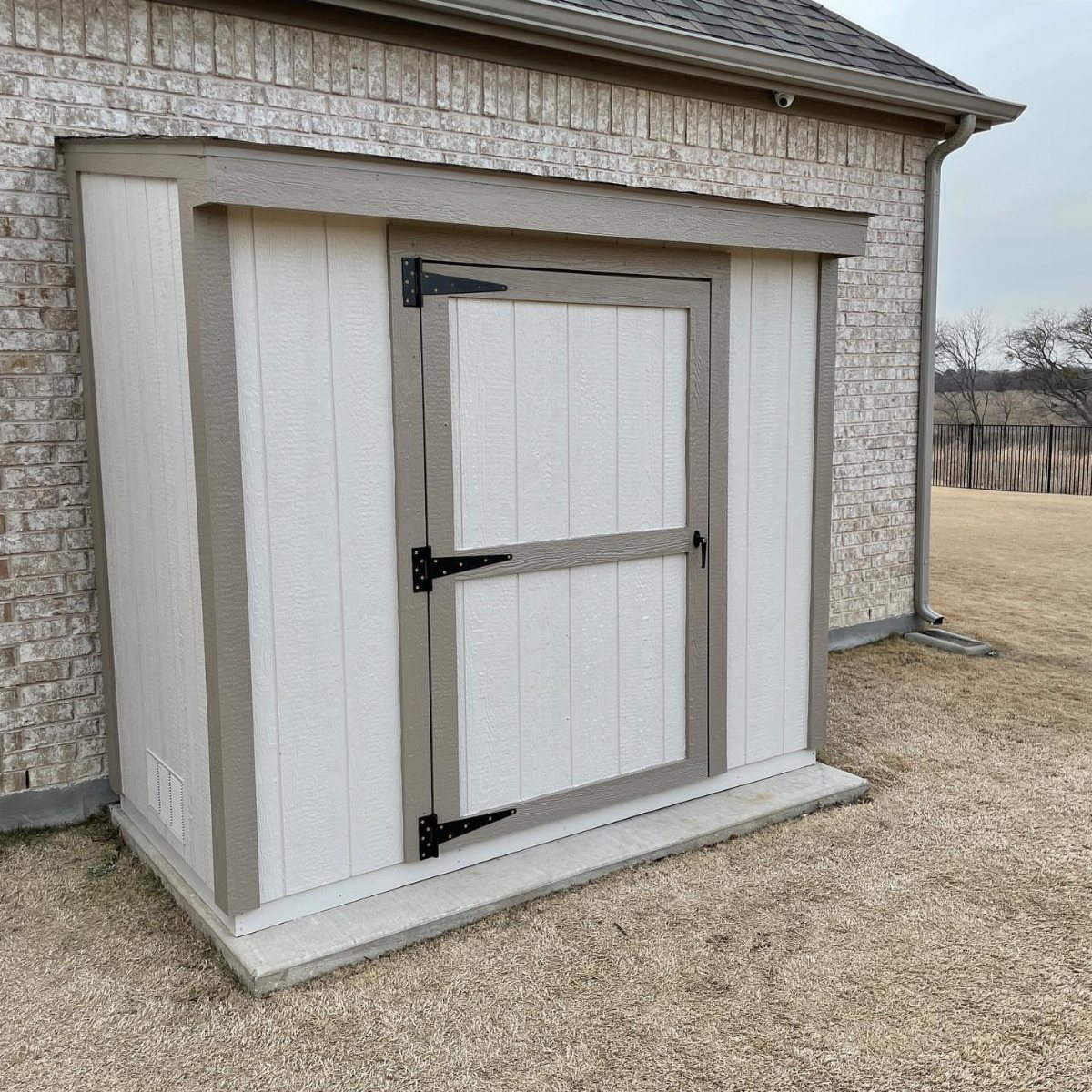 A white lean-to shed with tan trim attached to a brick building wall.