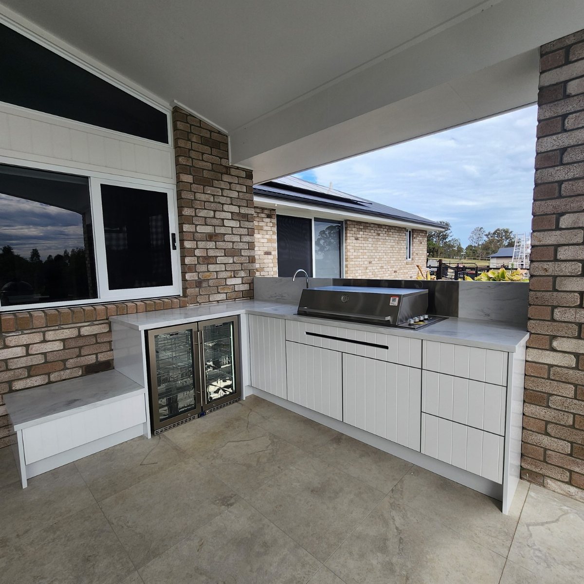 Modern outdoor kitchen with white cabinets, a built-in grill, and a small beverage fridge.