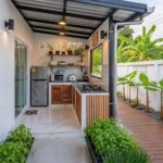 A compact outdoor kitchen with wooden cabinets, a small stove, and greenery under a black awning.